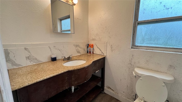 bathroom with toilet, vanity, and a textured wall