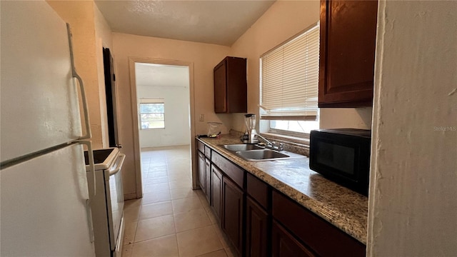 kitchen featuring dark brown cabinetry, light tile patterned floors, white appliances, and a sink