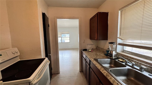 kitchen featuring dark brown cabinets, white electric range, light tile patterned flooring, and a sink