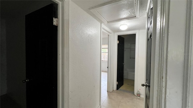 hall with light tile patterned flooring, a textured ceiling, and a textured wall