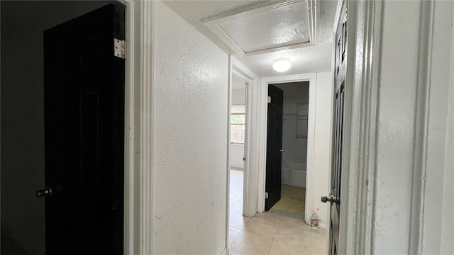 corridor featuring light tile patterned floors, a textured wall, and a textured ceiling