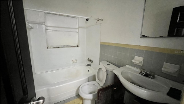 bathroom featuring tile patterned floors, toilet, tile walls, wainscoting, and washtub / shower combination