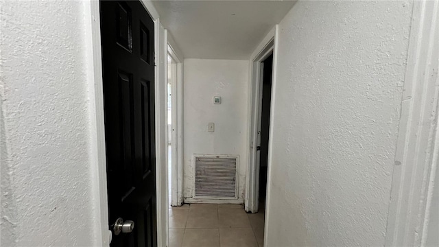 corridor featuring light tile patterned floors, visible vents, and a textured wall