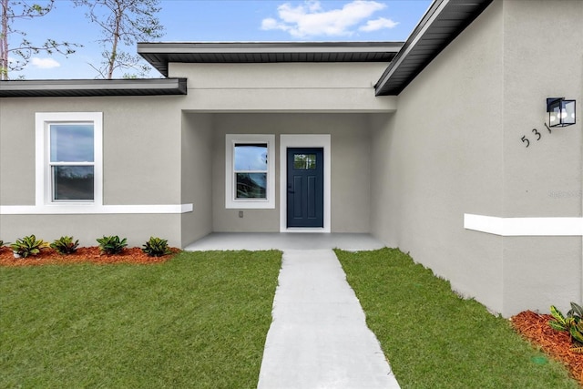 entrance to property featuring stucco siding and a lawn