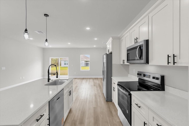 kitchen featuring a sink, light wood finished floors, white cabinetry, stainless steel appliances, and decorative light fixtures