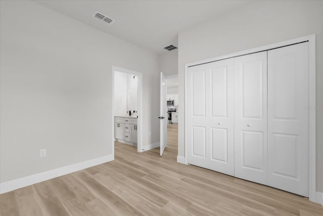 unfurnished bedroom with connected bathroom, a closet, baseboards, visible vents, and light wood-style floors