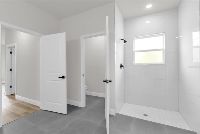bathroom with toilet, tiled shower, tile patterned flooring, and baseboards