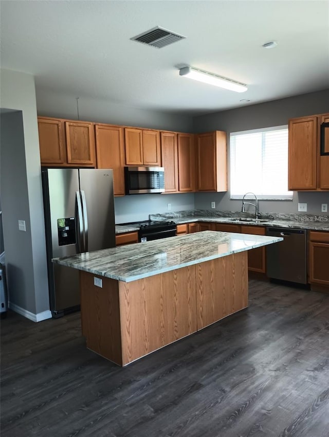 kitchen featuring visible vents, a sink, light stone counters, a center island, and stainless steel appliances