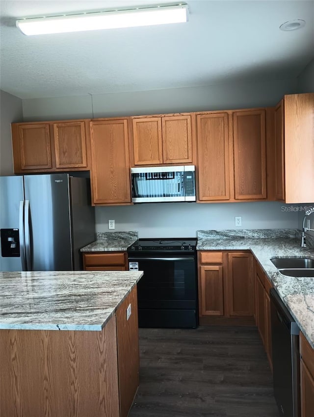 kitchen featuring a sink, light stone countertops, brown cabinets, appliances with stainless steel finishes, and dark wood-style flooring