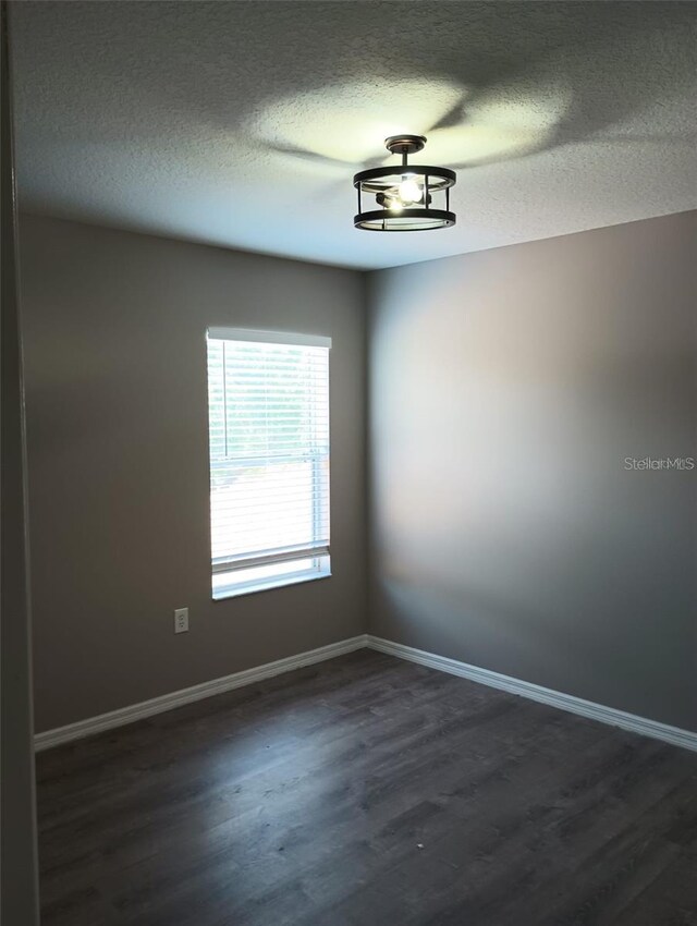 spare room featuring baseboards, a textured ceiling, and dark wood-style flooring