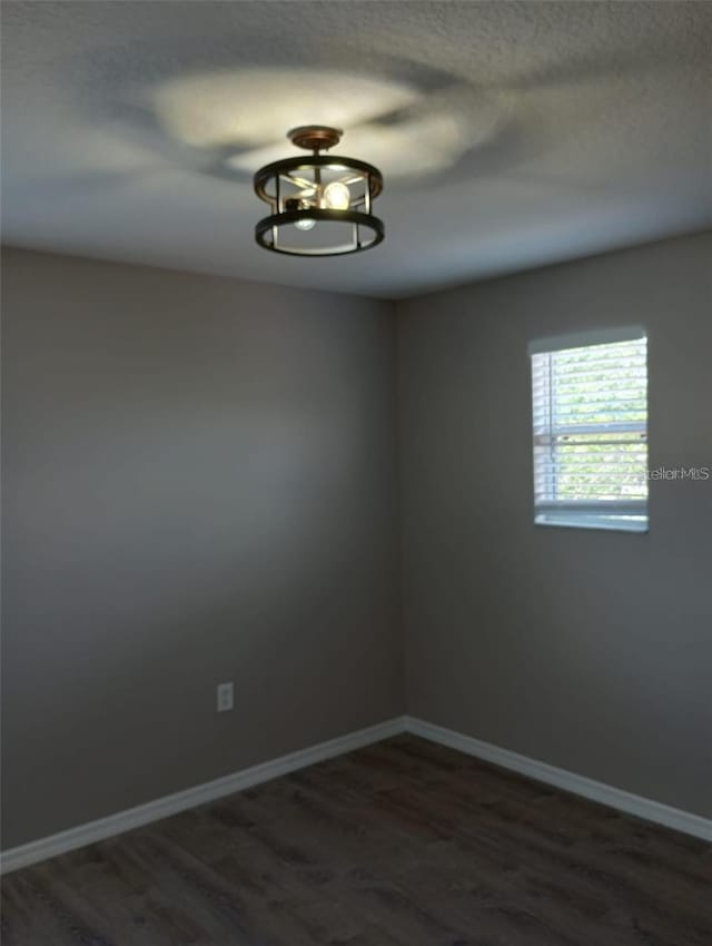 unfurnished room with a textured ceiling, dark wood-type flooring, and baseboards