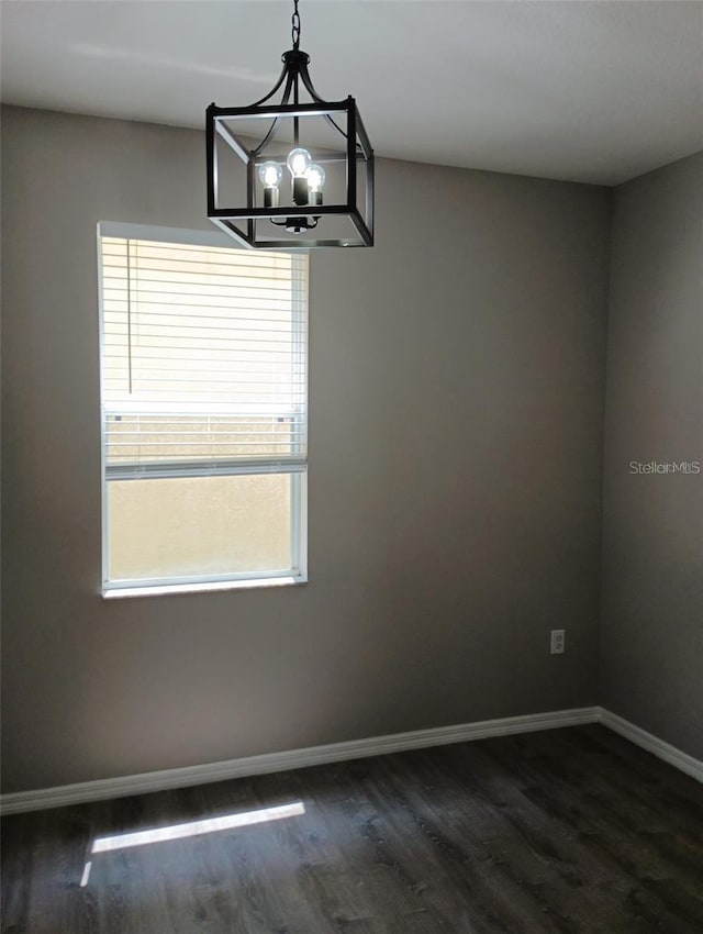 unfurnished room with baseboards, a notable chandelier, and dark wood finished floors