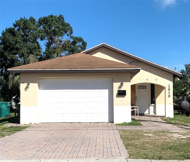 single story home with stucco siding, decorative driveway, roof with shingles, and an attached garage