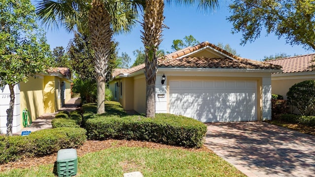 mediterranean / spanish-style home featuring stucco siding, an attached garage, a tile roof, and decorative driveway