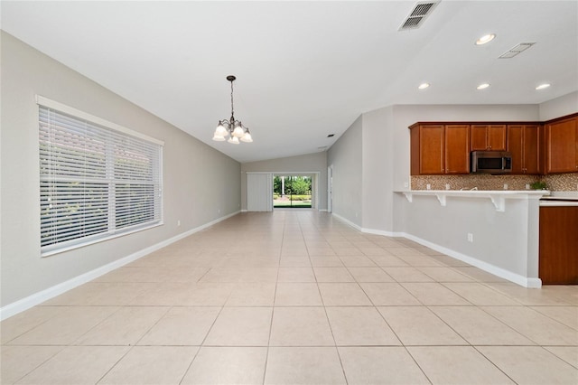 kitchen featuring stainless steel microwave, visible vents, open floor plan, a breakfast bar, and brown cabinetry