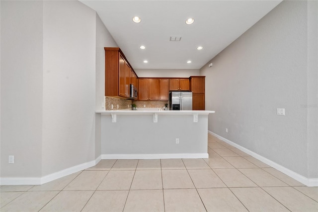 kitchen featuring a breakfast bar, a peninsula, stainless steel appliances, decorative backsplash, and light countertops