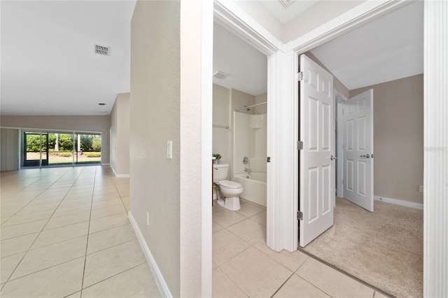 hallway featuring light tile patterned floors, visible vents, baseboards, and light carpet