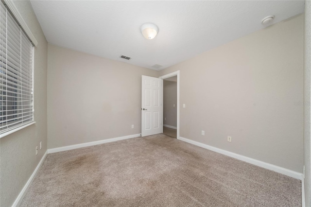 unfurnished bedroom featuring visible vents, light colored carpet, a textured ceiling, and baseboards