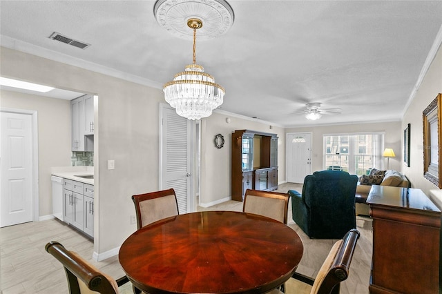 dining area with baseboards, visible vents, ornamental molding, light wood-style floors, and ceiling fan with notable chandelier