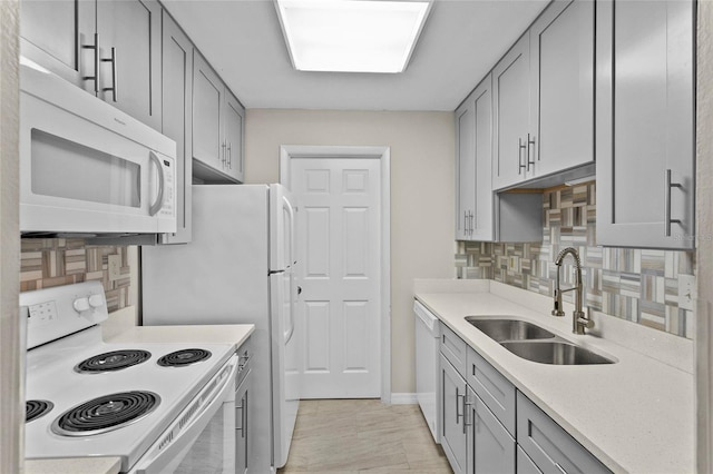 kitchen with decorative backsplash, white appliances, gray cabinetry, and a sink