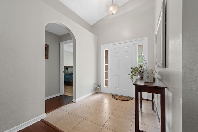 entrance foyer with arched walkways, light tile patterned floors, baseboards, and vaulted ceiling