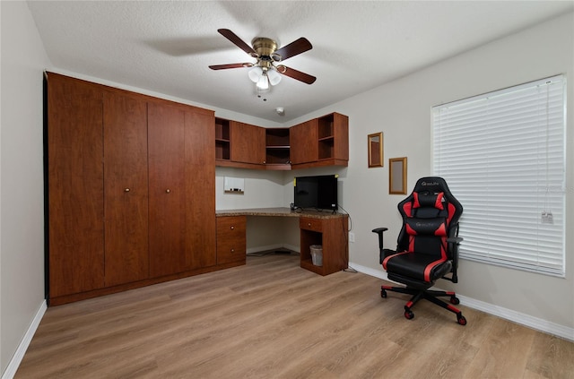 office featuring light wood-style flooring, baseboards, built in desk, and ceiling fan