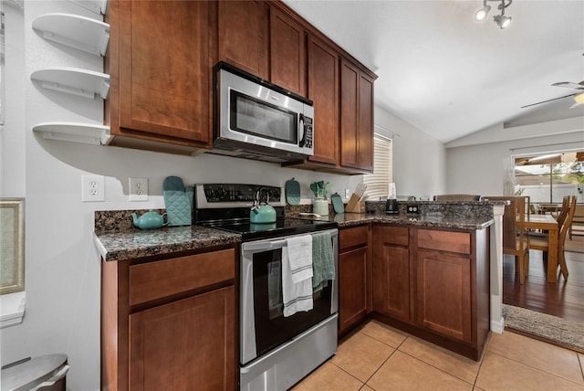 kitchen with dark stone counters, appliances with stainless steel finishes, a peninsula, and light tile patterned flooring