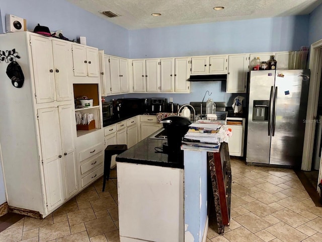 kitchen with visible vents, a sink, under cabinet range hood, stainless steel fridge, and a center island