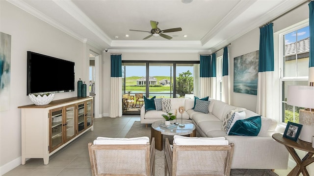 tiled living room featuring a tray ceiling, baseboards, a ceiling fan, and crown molding