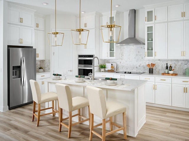 kitchen featuring a center island with sink, stainless steel appliances, wall chimney exhaust hood, white cabinets, and light countertops