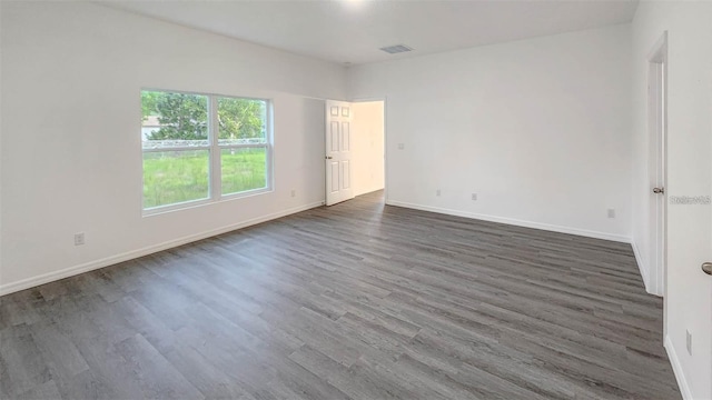 unfurnished room with baseboards, visible vents, and dark wood-style flooring