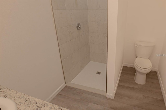 bathroom featuring baseboards, toilet, wood finished floors, and a tile shower