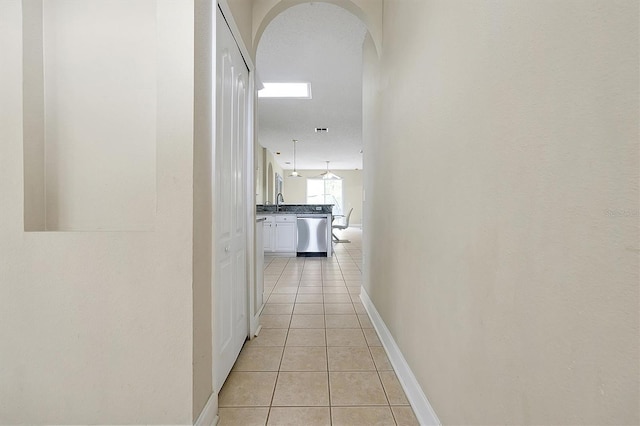 hall with light tile patterned floors, baseboards, arched walkways, and a sink