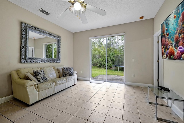 living area featuring visible vents, baseboards, ceiling fan, light tile patterned flooring, and a textured ceiling