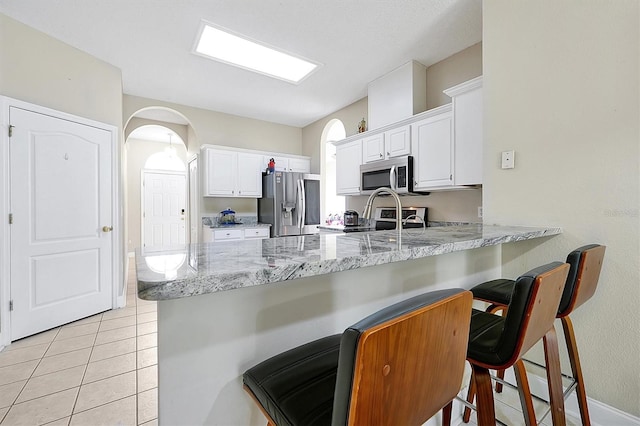 kitchen featuring a breakfast bar, a peninsula, arched walkways, white cabinets, and stainless steel appliances