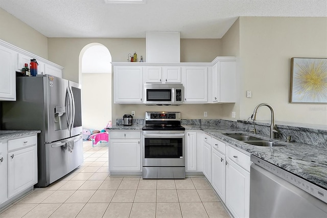 kitchen with a sink, light stone counters, stainless steel appliances, white cabinets, and light tile patterned floors