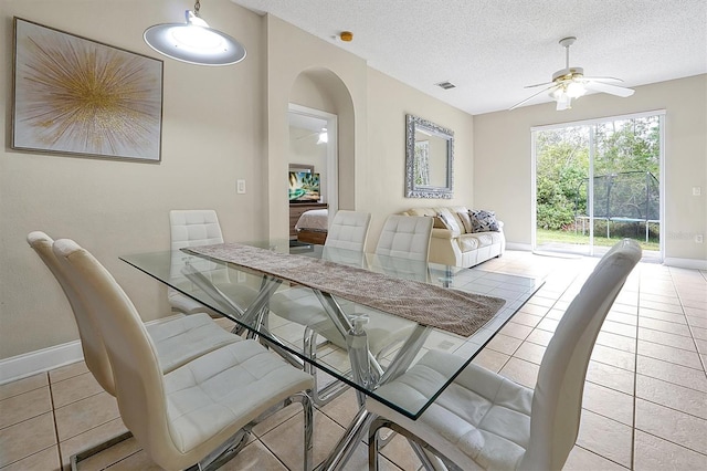 dining room featuring baseboards, ceiling fan, arched walkways, light tile patterned flooring, and a textured ceiling