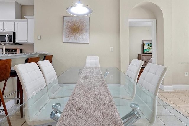 dining space featuring light tile patterned flooring, arched walkways, and baseboards