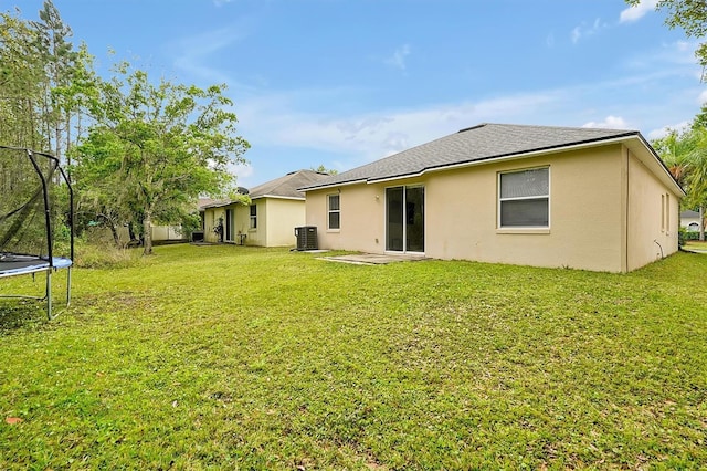 rear view of property with a yard, stucco siding, cooling unit, and a trampoline