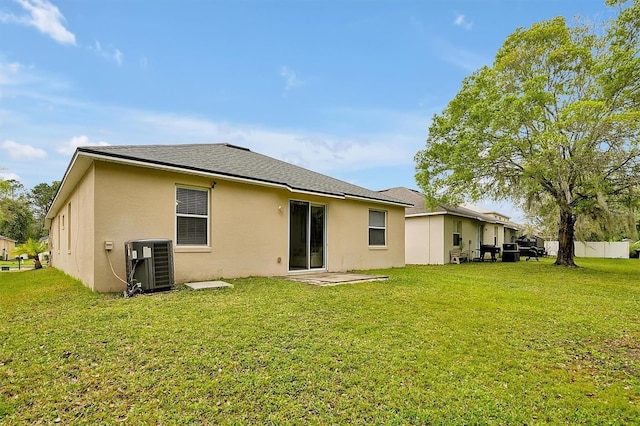 rear view of house with cooling unit, a lawn, fence, and stucco siding