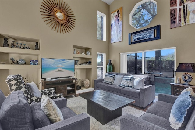 living room with built in shelves, wood finished floors, and a towering ceiling