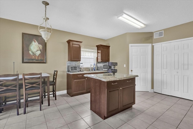 kitchen featuring visible vents, a kitchen island, light tile patterned flooring, stainless steel microwave, and tasteful backsplash