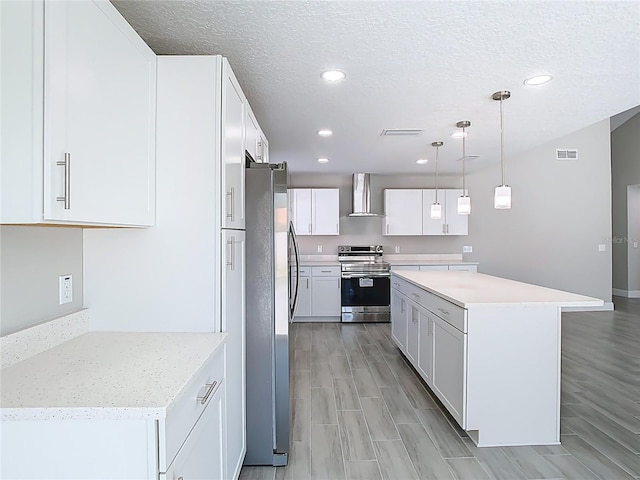 kitchen with visible vents, a kitchen island, stainless steel appliances, white cabinetry, and wall chimney range hood