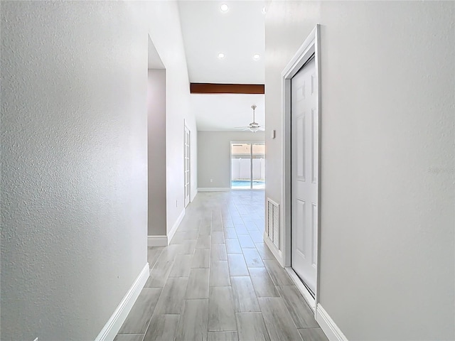 hallway with wood finish floors, visible vents, baseboards, and beam ceiling