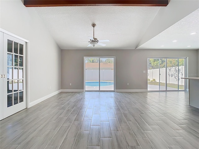 spare room featuring lofted ceiling with beams, plenty of natural light, a textured ceiling, and ceiling fan