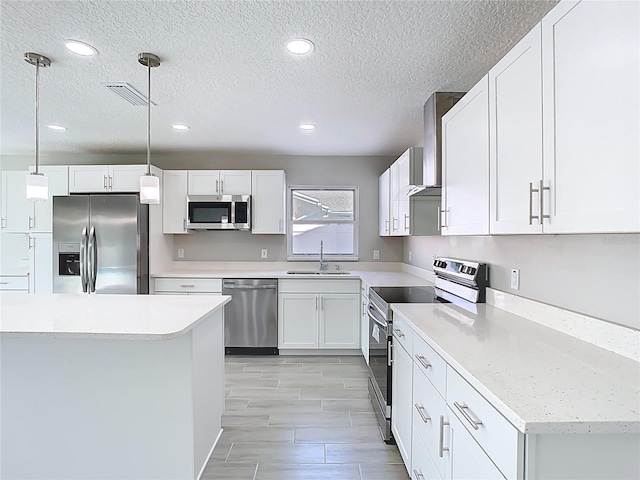 kitchen featuring visible vents, appliances with stainless steel finishes, white cabinetry, wall chimney exhaust hood, and a sink