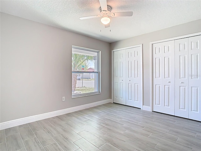 unfurnished bedroom with ceiling fan, baseboards, multiple closets, light wood-style floors, and a textured ceiling