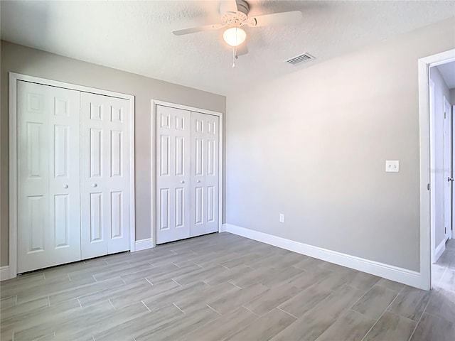 unfurnished bedroom with wood finish floors, visible vents, baseboards, and two closets