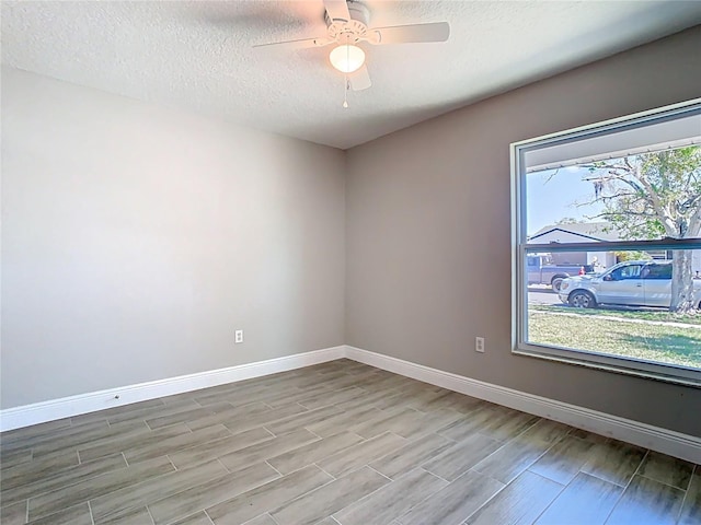 spare room with a textured ceiling, a ceiling fan, baseboards, and wood finish floors