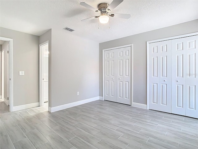 unfurnished bedroom with wood finish floors, baseboards, visible vents, and multiple closets